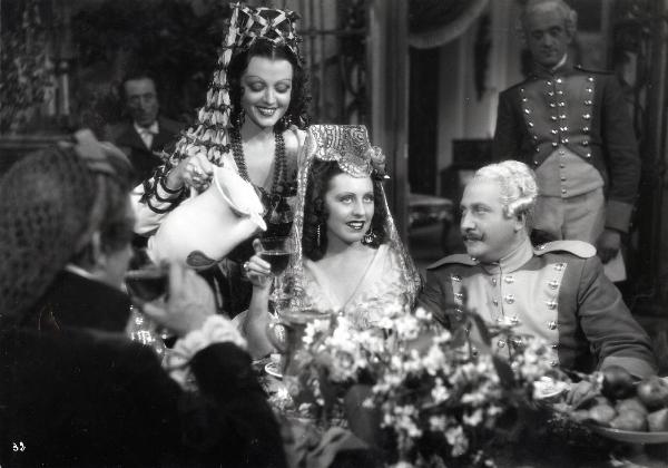 Scena del film "Elisir d'amore" - Regia Amleto Palermi, 1941 - Margherita Carosio, al centro, si fa riempire un bicchiere da un'attrice non identificata. Attorno, altri attori non identificati la osservano.
