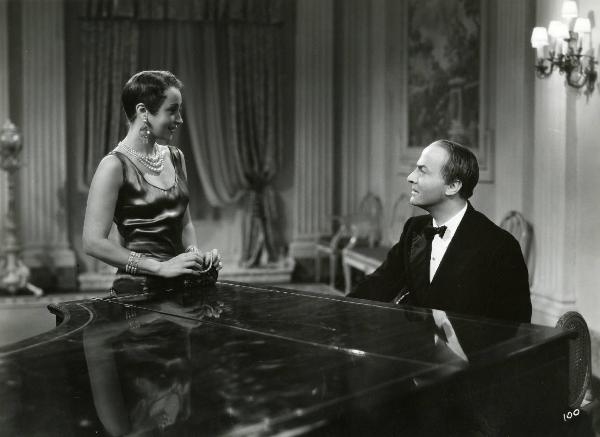 Scena del film "Enrico IV" - Regia Giorgio Pastina, 1943 - A destra, Osvaldo Valenti seduto a un pianoforte, osserva Clara Calamai, a sinistra, che ricambia il suo sguardo.