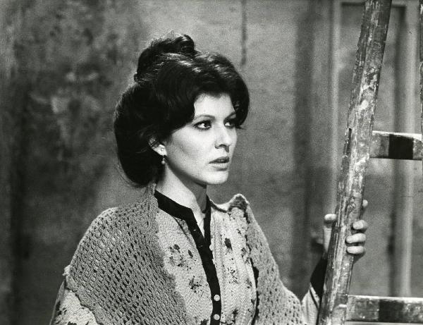 Scena del film "Er più storia d'amore e di coltello" - Regia Sergio Corbucci, 1971 - Primo piano di Claudia Mori che, poggiando la mano sinistra su una scala in legno, rivolge lo sguardo a destra.