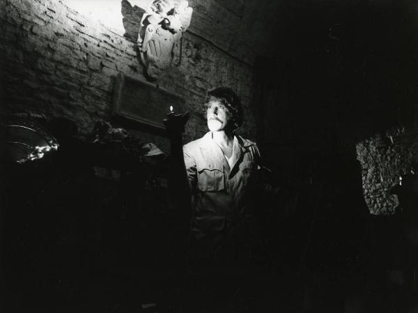 Scena del film "L'etrusco uccide ancora" - Regia Armando Crispino, 1972 - Al buio, Alex Cord rivolge lo sguardo verso sinistra, sorreggendo nella mano destra una fonte di luce a fiamma.