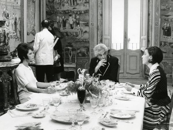 Scena del film "L'etrusco uccide ancora" - Regia Armando Crispino, 1972 - In una sala da pranzo, seduti a un tavolo: Samantha Eggar, a sinistra, John Marley, al centro che si porta una sigaretta alla bocca e un'attrice non identificata, a destra.