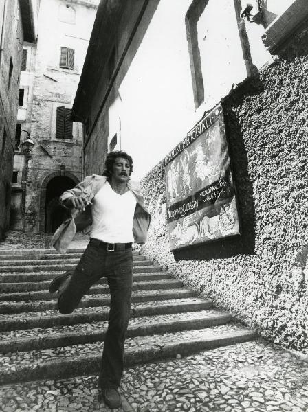 Scena del film "L'etrusco uccide ancora" - Regia Armando Crispino, 1972 - Figura intera di Alex Cord che scende correndo da una scalinata affiancata da un muro con un manifesto che riporta la dicitura "IMMAGINI MEDIOEVALI".