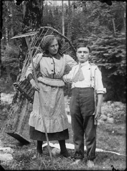 Val Brembana. Ritratto di una giovane coppia nel bosco: lei contadina con gerla e rastrello e lui carrettiere con la fune in mano