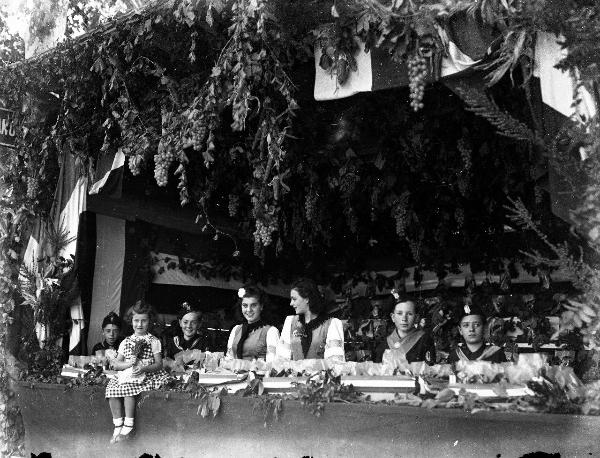 Ritratto di gruppo - Tre giovani donne in abiti tradizionali in piedi su un'autovettura addobbata di fiori, alla guida un signore - Salice Terme - IX Festa nazionale dell'uva