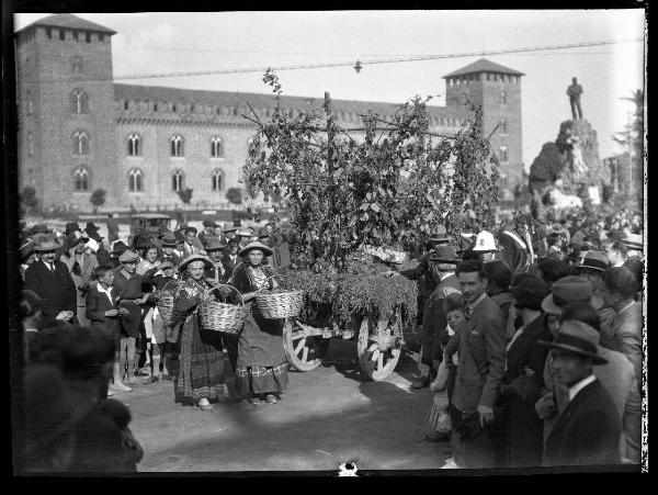 Ritratto di gruppo femminile - Due giovani donne con abiti tradizionali, cappelli e cesti di vimini in mano, circondate da una folla di persone - Carro con grappoli e tralci d'uva - Pavia - Piazza Castello - 3Â° festa dell'uva