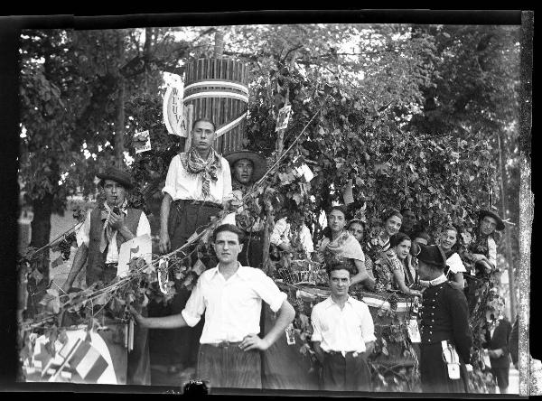 Ritratto di gruppo - Gruppo di uomini e giovani donne in abiti tradizionali sul carro, addobbato con tralci di vite e grappoli d'uva e fasce tricolori, è rappresentato un fascio littorio - Pavia - 3° Festa nazionale dell'uva