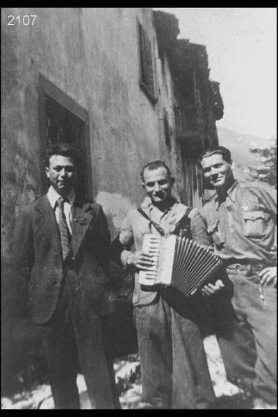 Egidio Angiolini, Ambrogio Manzoni detto 'scinca', Antonio Vitari detto 'marsenta'. Posa davanti a edifici di campagna. L'uomo al centro suona la fisarmonica.