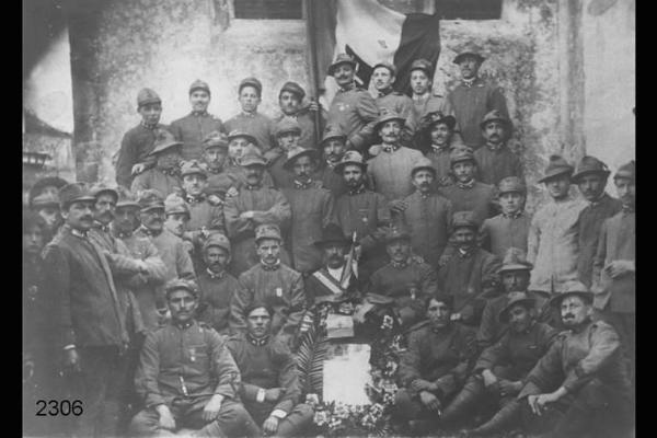 Reduci della prima guerra mondiale. Posa di gruppo in esterno con corona di fiori e bandiera sabauda.