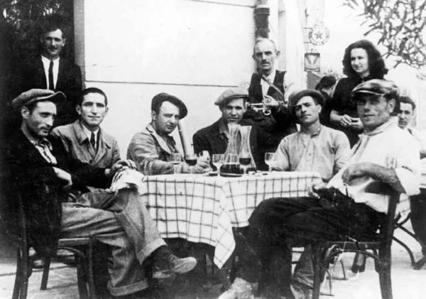 Ritratto di gruppo intorno ad un tavolo imbandito. Il secondo seduto è Giovanni Mazzoleni, ambulante alimentare.