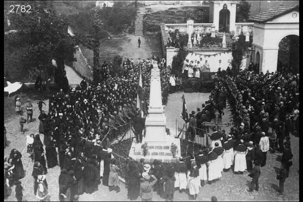 Inaugurazione del monumento ai Caduti a Rota Fuori. Panoramica della piazza col monumento e civili, militari, confraternita e religiosi intorno ad esso; sullo sfondo il camposanto.