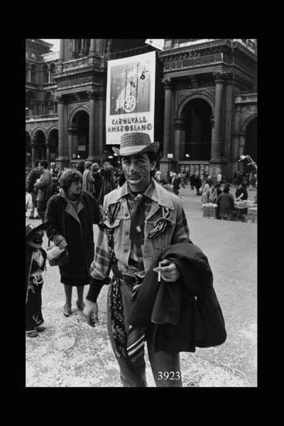 Uomo in costume in piazza Duomo: in mano tiene una sigaretta e sul braccio un soprabito.