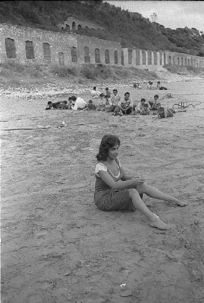 Rodi Garganico. Spiaggia. Set del film "La legge", diretto da Jules Dassin. Gina Lollobrigida, seduta sulla sabbia, lancia sassi nel mare