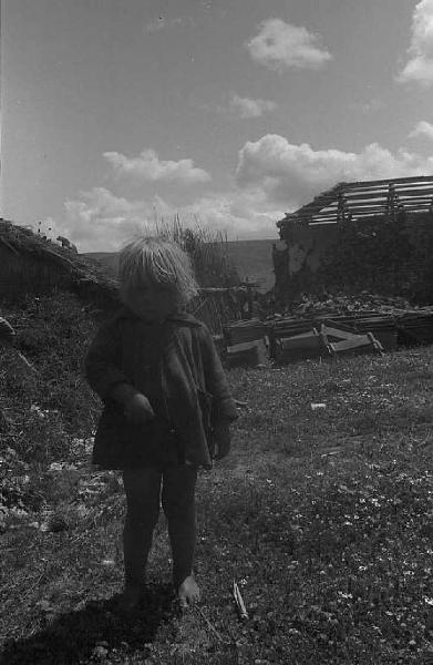 Località non identificata.Terremoto. Ritratto di bambino. Sullo sfondo le macerie di una casa distrutta dal sisma