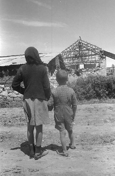 Località non identificata.Terremoto. Coppia di bambini per mano osservano le macerie di una casa distrutta dal sisma