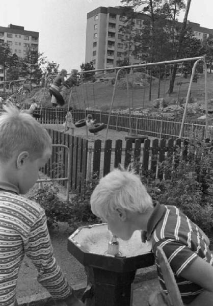 Svezia - Due bambini bevono alla fontanella di un parco giochi cittadino - Sullo sfondo palazzi di periferia