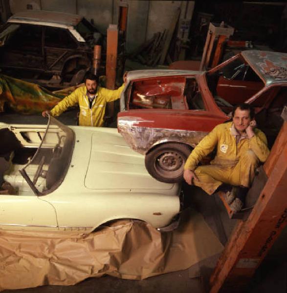 Autofficina macchine sportive - due maestranze posano di fianco a una vettura durante una fase della lavorazione