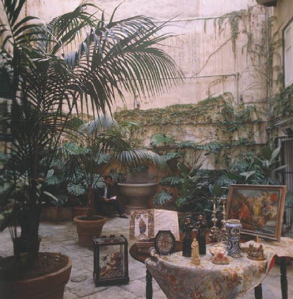 Ritratto dell'antiquario Marcello Raspanti seduto fra gli oggetti d'antiquariato esposti in una corte interna