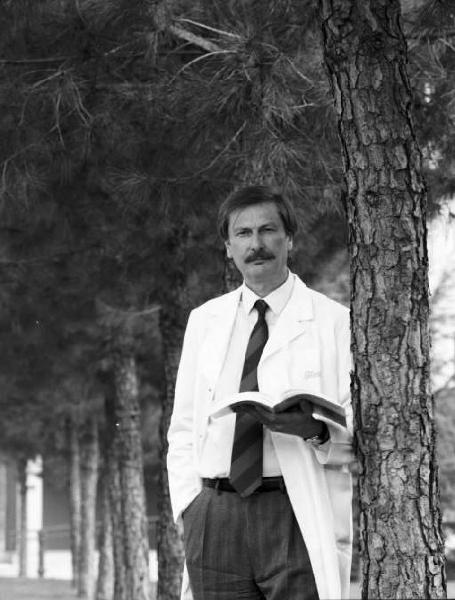 Glaxo - Ritratto di un medico con camice bianco slacciato e libro aperto in mano sotto un pino