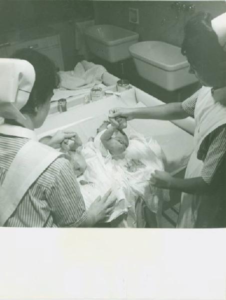 Ritratto di gruppo - Neonati con due infermiere durante il cambio del pannolino