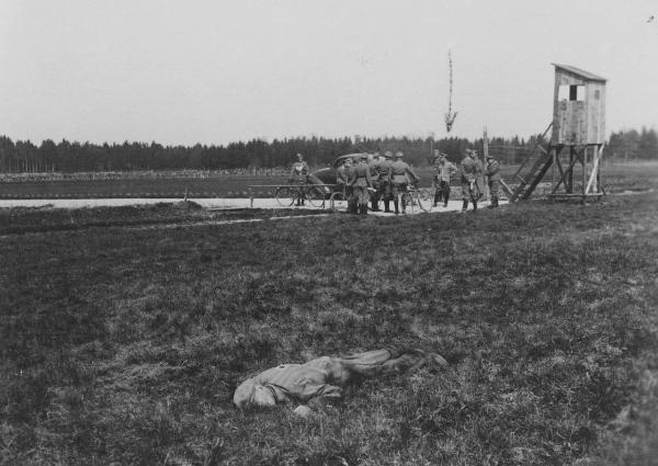 Seconda guerra mondiale - Nazismo - Germania - Campo di concentramento di Dachau - Prigioniero ucciso a terra dopo una tentata fuga - SS in divisa con bicicletta - Torretta di avvistamento