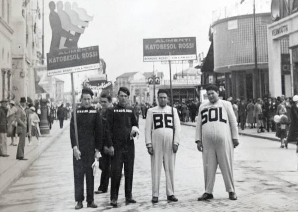 Fiera di Milano - Campionaria 1934 - Quattro uomini con abbigliamento e cartelli pubblicitari degli alimenti Katobesol Rossi