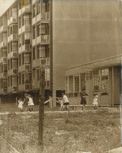 Milano - Quartiere Chiesa Rossa - Bambini giocano all'esterno della scuola materna - Palazzi sullo sfondo - Edificio prefabbricato - Terreno incolto