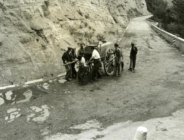 Scena del film "Fari nella nebbia" - Regia Franciolini, Gianni, 1942 - Un gruppo di attori non identificati sono intenti a tirare un carro lungo una strada di montagna in salita.