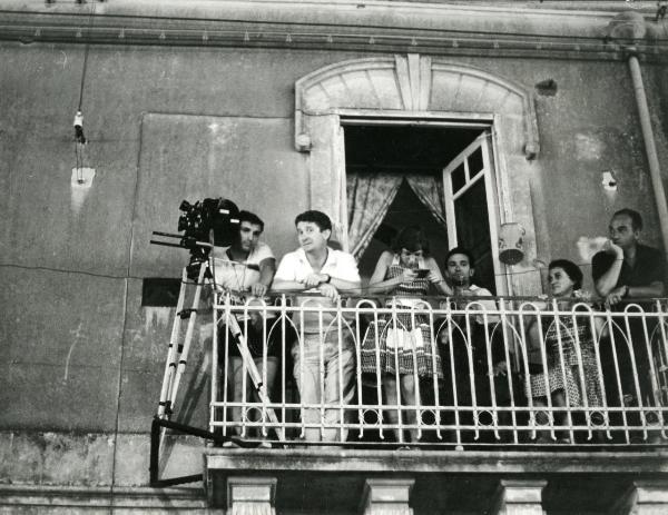 Sul set del film "I fidanzati" - Olmi, Ermanno, 1963 - Su un balcone, operatori non identificati rivolgono lo sguardo verso l'obbiettivo. A cavallo con la balaustra sinistra del balcone è presente una macchina da presa.
