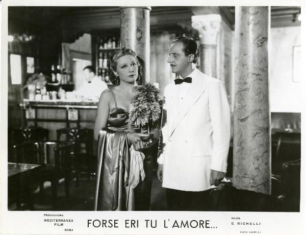 Scena del film "Forse eri tu l'amore" - Righelli, Gennaro, 1939 - I due protagonisti Loretta Vinci e Sandro Ruffini in una scena d'interno. Lei vestita da sera guarda dritto davanti a sé, mentre lui di fianco, la fissa.
