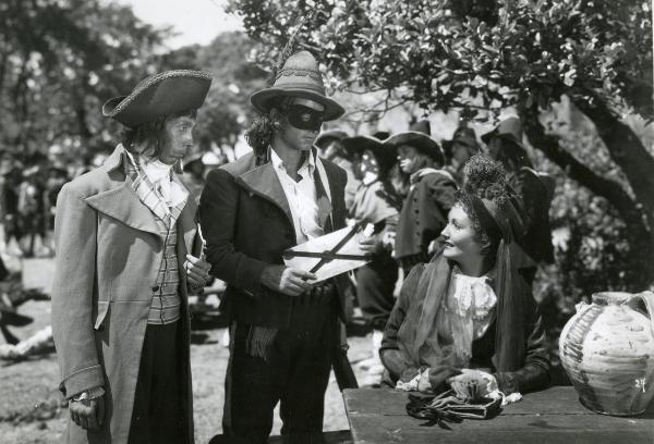 Scena del film "Fra Diavolo" - Zampa, Luigi, 1942 - Laura Nucci seduta a un tavolo è rivolta verso sinistra dove guarda Enzo Fiermonte in maschera che le consegna un pezzo di carta. Di fianco a lui, un attore non identificato li guarda. 
