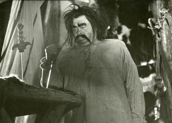 Scena del film "Francesco, giullare di Dio" - Rossellini, Roberto, 1950 - Aldo Fabrizi, con lo sguardo rivolto verso il basso, punta un pugnale su una superficie di legno.