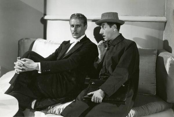Scena del film "Fuochi d'artificio" - Righelli, Gennaro, 1938 - A sinistra, Amedeo Nazzari che con le mani conserte si tiene il ginocchio sinistro e ascolta Giuseppe Porelli, a destra, mentre tiene con la mano sinistra una valigetta.