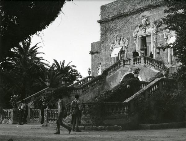 Scena del film "Il gattopardo" - Visconti, Luchino, 1963 - Davanti al cortile di una villa, alcuni attori non identificati nei panni di giardinieri guardano verso il piano rialzato dell'edificio dove, al centro, si riconosce Burt Lancaster.