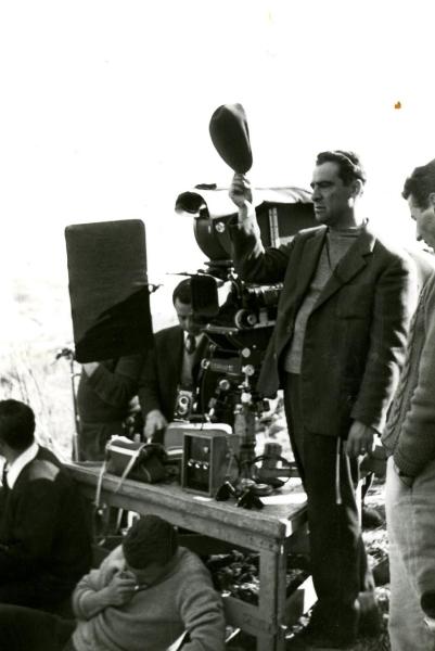 Fotografia sul set di "Un giorno da leoni" - Loy, Nanni, 1961 - Marcello Gatti, con una coppola nella mano destra, mentre gira insieme ad operatori non identificati una scena del film.