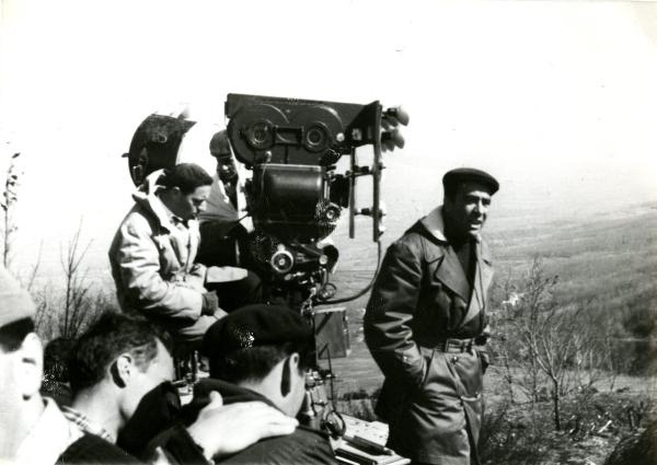 Fotografia sul set di "Un giorno da leoni" - Loy, Nanni, 1961 - Marcello Gatti, davanti alla cinepresa, parla mentre guarda a destra. Attorno, operatori non identificati.