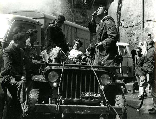 Fotografia sul set di "Un giorno da leoni" - Loy, Nanni, 1961 - Su una automobile: un'attrice non identificata, Nanni Loy, un attore non identificato e Marcello Gatti che guarda in alto con una lente. Attorno operatori non identificati.