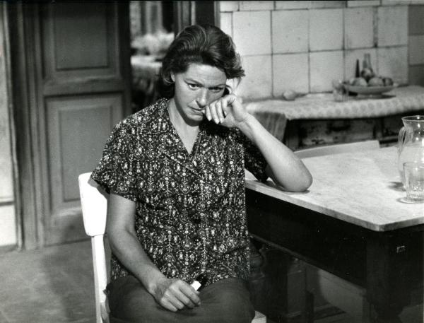 Scena del film "Giorno per giorno disperatamente" - Giannetti, Alfredo, 1961 - Su una sedia è seduta Madeleine Robinson. L'attrice, guardando verso il basso, poggia la testa alla mano sinistra mentre nella mano destra tiene in mano un oggetto.