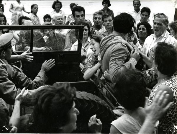 Scena del film "Giorno per giorno disperatamente" - Giannetti, Alfredo, 1961 - Al centro, Madeleine Robinson spinge un attore non identificato di spalle su una macchina militare. Attorno, una folla di attori non identificati.