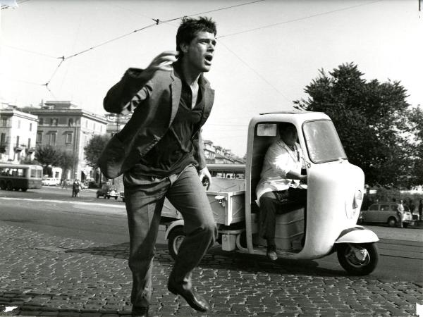 Scena del film "Giorno per giorno disperatamente" - Giannetti, Alfredo, 1961 - Figura intera di Nino Castelnuovo mentre corre. Dietro di lui, un'ape con alla guida un attore non identificato.