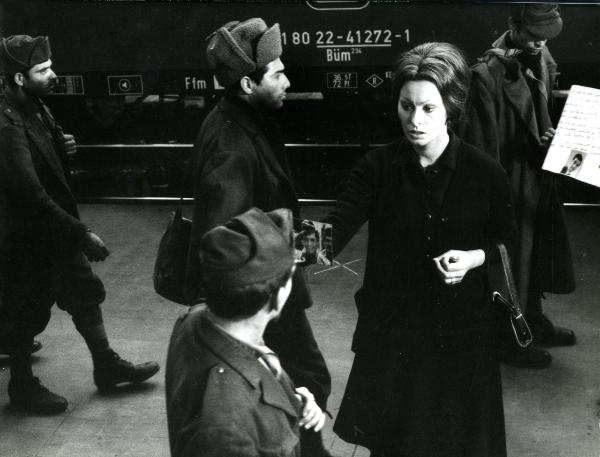 Scena del film "I girasoli" - De Sica, Vittorio, 1970 - Sulla Banchina di un treno, Sophia Loren, tenendo nella mano destra una fotografia, chiede informazioni a un soldato di fronte a lei. Dietro l'attrice, altri soldati non identificati.