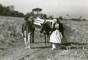 Fotografia sul set di "Un garibaldino al convento" - De Sica, Vittorio, 1942 - A sinistra il registra Vittorio De Sica mentre a destra Carla Del Poggio. Lei tiene le redini di un asino dietro di lei. Lui guarda verso l'attrice.