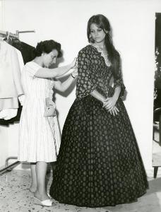 Fotografia sul set di "Il gattopardo" - Visconti, Luchino, 1963 - A destra, Claudia Cardinale mentre si fa sistemare il vestito di scena da una sarta, a sinistra.