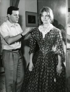 Fotografia sul set di "Il gattopardo" - Visconti, Luchino, 1963 - A destra, Claudia Cardinale mentre si fa sistemare il vestito di scena da Piero Toti, il costumista.