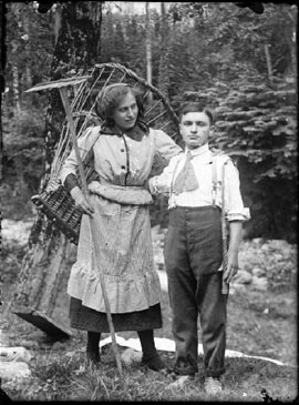 Goglio, Eugenio - Val Brembana. Ritratto di una giovane coppia nel bosco: lei contadina con gerla e rastrello e lui carrettiere con la fune in mano
