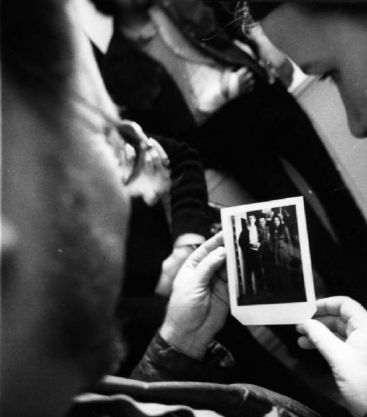 Coppia di persona osserva polaroid che li raffigura accanto alla sagoma bidimensionale dell'autore