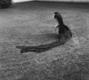 Donna nuda cammina sull'erba trascinando un lungo drappo