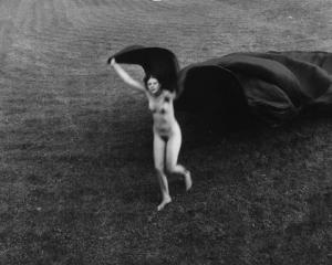 Donna nuda corre sull'erba muovendo un lungo drappo