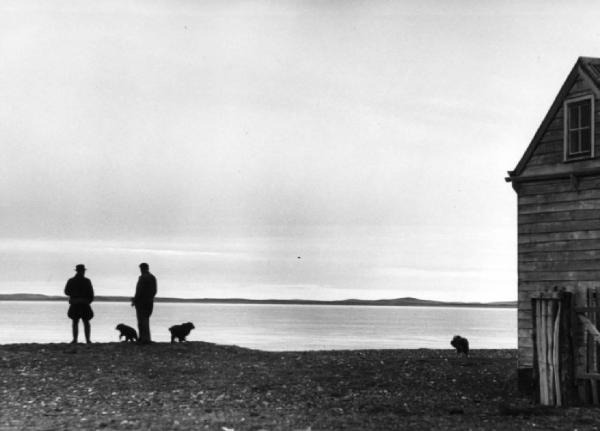 Coppia di uomini con cani nei pressi di un capanno in riva a un lago