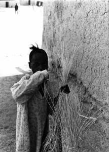 Fanciulla di colore con in mano fasci di fieno appoggiata a un muro di fango
