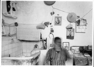 Interni mossi. Interno domestico - lavatoio - santini appesi a parete - figura umana in movimento - autoritratto di Mario Cresci